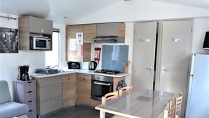 Cocina compacta con microondas, estufa y cafetera. Hay una mesa de comedor con sillas y un pequeño sofá.