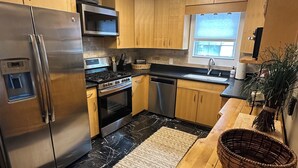 Une cuisine moderne dotée d’appareils électroménagers en acier inoxydable, de meubles en bois, d’un sol en marbre noir et blanc et d’une grande fenêtre qui laisse entrer la lumière naturelle.