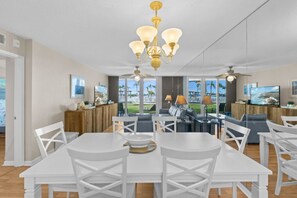 Un comedor amplio con mobiliario blanco, una araña y vistas al exterior.