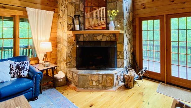 A cozy cabin interior with a stone fireplace, wooden ceiling, and large windows.