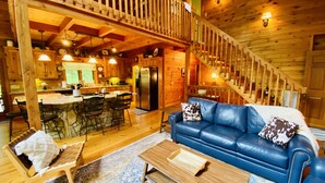A spacious cabin interior with a dining area, kitchen, and a blue leather sofa with a patterned pillow.