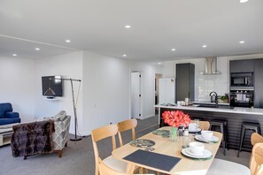 A modern kitchen with a central island, a dining area with a table set for four, and a living room with a sofa and a television.