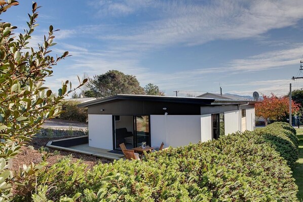 A modern house with a flat roof, a patio with outdoor furniture, and a well-maintained garden.