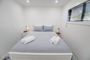 A neatly made bed with white linens, two bedside tables with lamps, and a window with blinds.