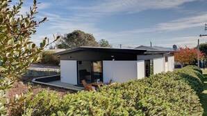 Ein modernes, eingeschossiges Haus mit flachem Dach, großen Glasfenstern und einer Terrasse mit Gartenmöbeln.