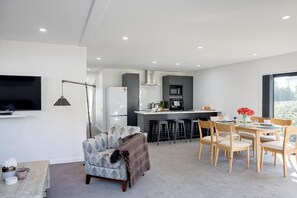 A modern living room with a sofa, a dining table with chairs, a kitchen area with a fridge, microwave, and bar stools.