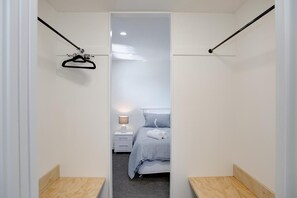 Ein schmaler Flur führt zu einem Schlafzimmer mit einem Bett, einem Nachttisch und einem Kleiderhaken.