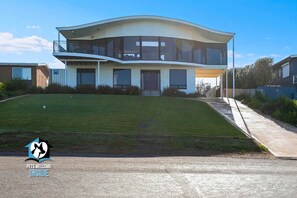 A modern two-story house with a curved roof, large windows, and a well-maintained lawn.