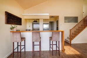 Une cuisine avec un coin bar, des chaises en bois, un luminaire suspendu et un escalier.