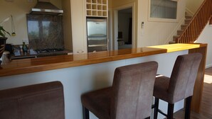 A kitchen with a marble countertop, stainless steel appliances, and a wooden staircase. - Ahi Apartment  with Tasman Sea views (Raglan)
