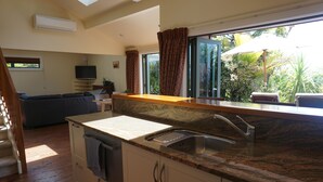 A modern kitchen with a granite countertop, a built-in sink, and a large window with curtains. - Ahi Apartment  with Tasman Sea views (Raglan)