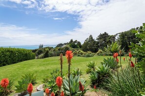 A well-maintained garden with a variety of plants and a view of the sea. - Ahi at Koru Lodge – Private Spa Pool & Sea Views (Raglan)