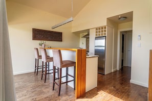 A kitchen with a central island, bar stools, a stainless steel refrigerator, and a hanging light fixture.