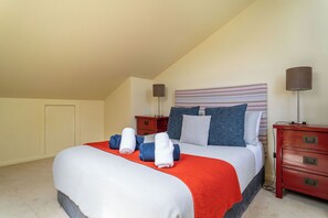 Una cama bien hecha con una manta roja, almohadas y toallas enrolladas. Hay dos mesitas de noche con lámparas y un aparador rojo con cajones.