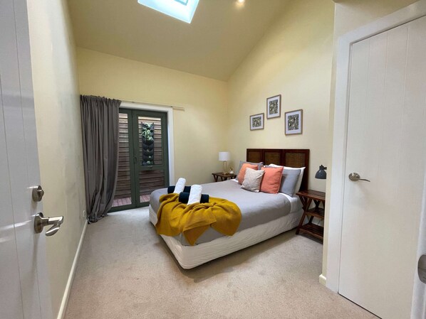 A bedroom with a bed, a nightstand, a lamp, a door, and a window.