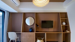 Un dormitorio moderno con escritorio empotrado, espejo redondo, televisor de pantalla plana y una silla.
