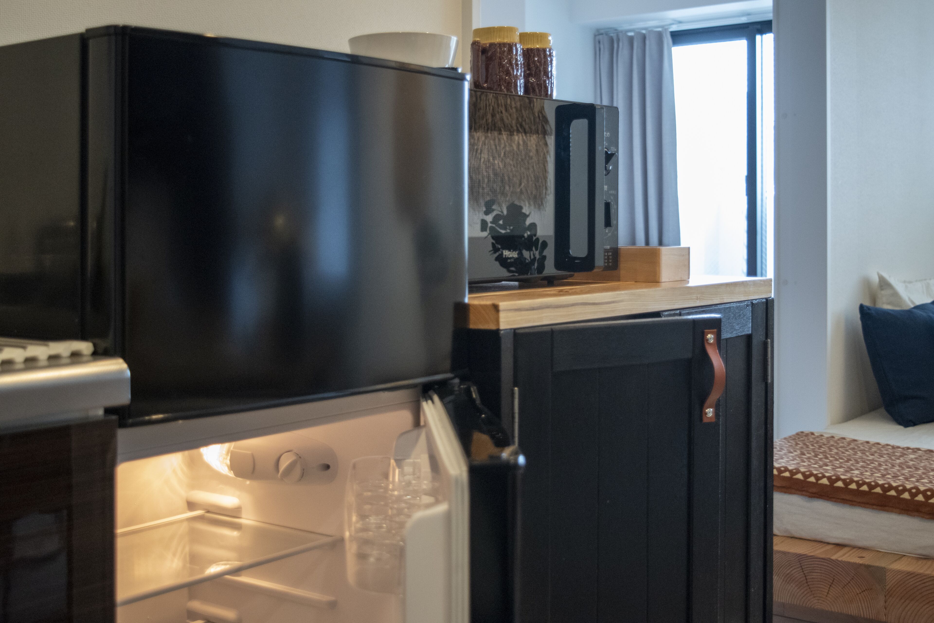 A compact kitchen with a refrigerator, microwave, and a small countertop with jars.
