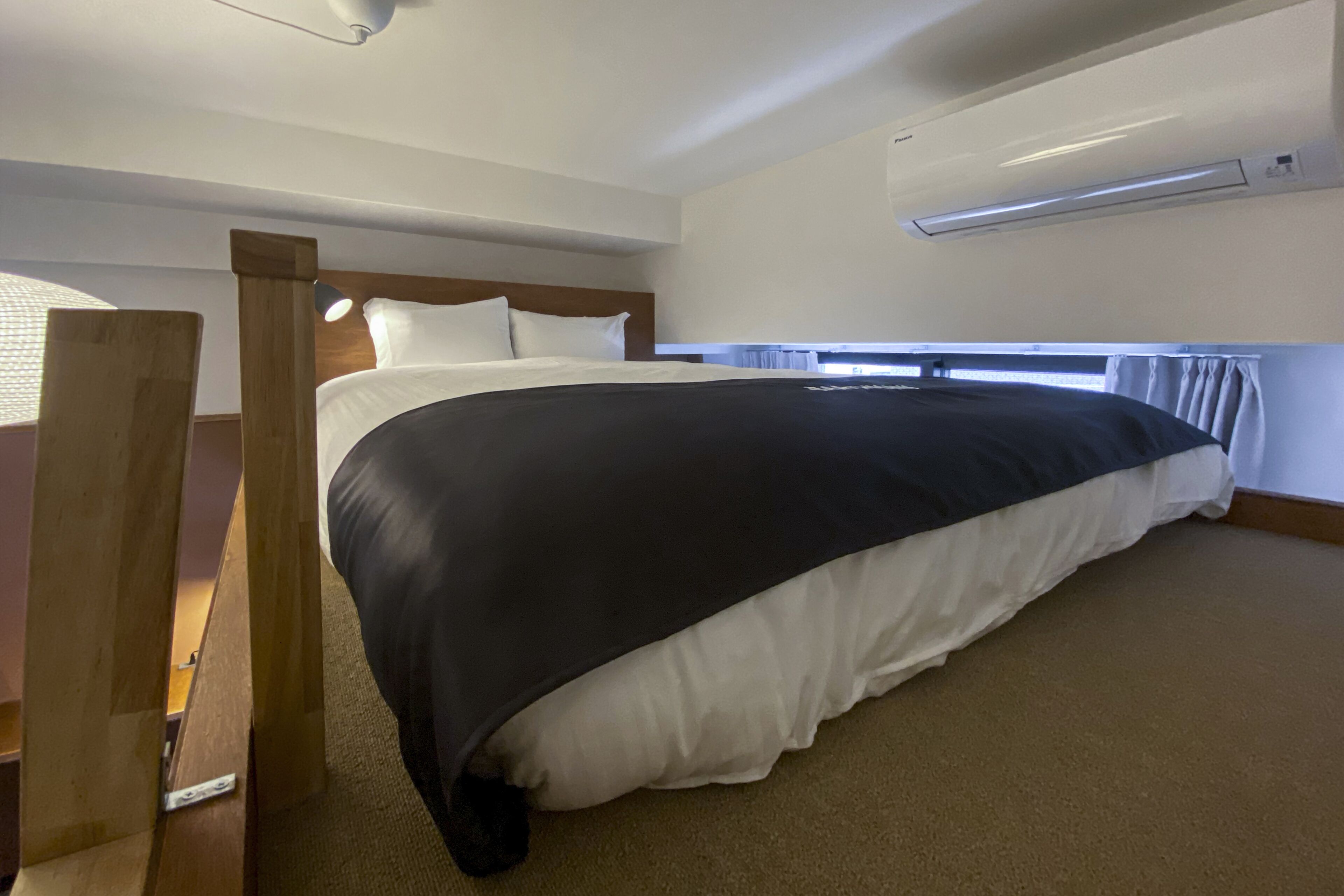Una habitación de hotel con una cama grande, cabecero de madera, ropa de cama blanca y un equipo de aire acondicionado instalado en el techo.