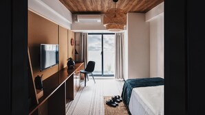 Una habitación de hotel moderna con techo de madera, televisor de pantalla plana, escritorio, silla, cama y ventana grande con cortinas.