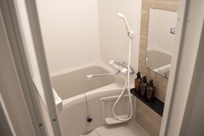 A modern bathroom with a bathtub, shower, and a vanity with bottles. - EARTHMANS Osaka-Jo (Osaka)