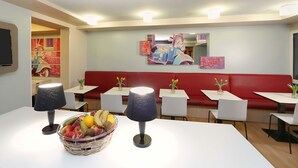 Een restaurant met witte tafels, rode banken en kunst aan de muren.