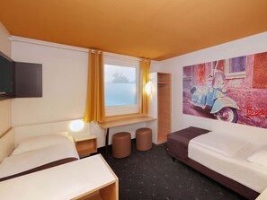 Ein Hotelzimmer mit zwei Betten, einem Vorhangfenster, einem an der Wand montierten Fernseher, einem kleinen Tisch und einem Gemälde eines Oldtimers.