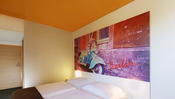 Een hotelkamer met een bed, een schilderij van een klassieke auto aan de muur en een deur.