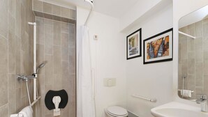 Een badkamer met een douche, toilet, wastafel en twee afbeeldingen in lijsten aan de muur.