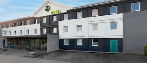 Un hotel moderno con techo plano, amplias ventanas y un área de entrada pavimentada.