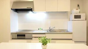 A modern kitchen with white cabinets, a stainless steel range hood, a microwave, and a sink. - Shin-Osaka GRAND (Osaka)