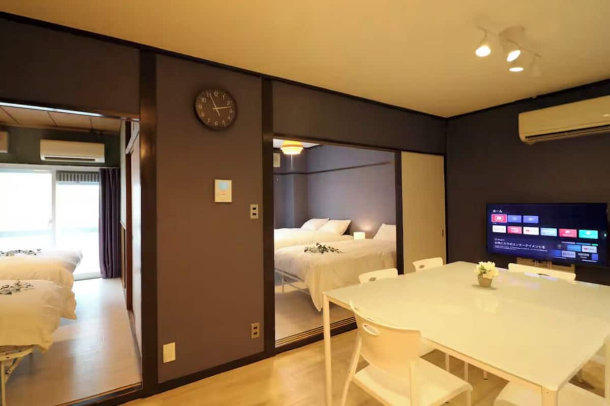 A hotel room with a bed, a TV, a dining table, and a clock on the wall.