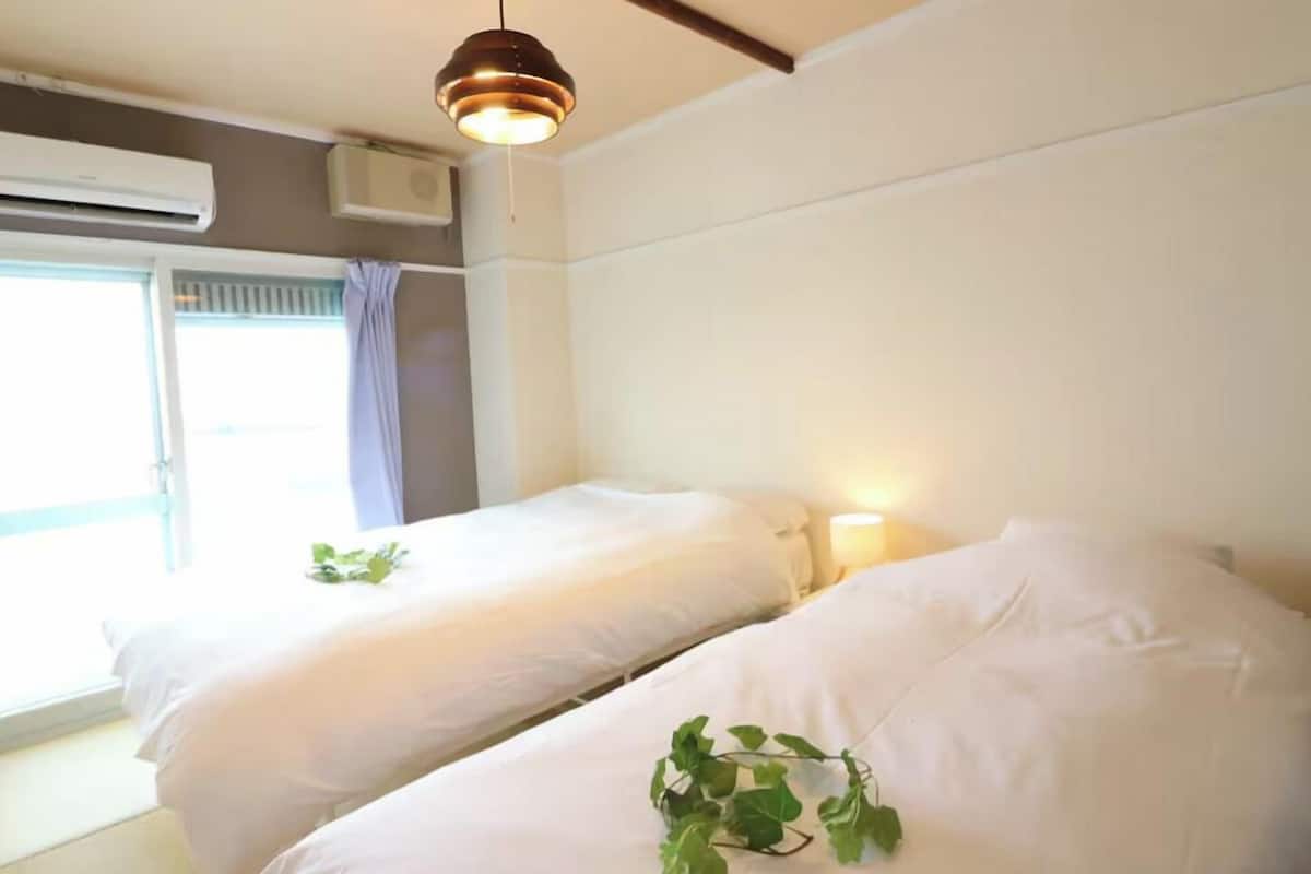 A room with two beds, a window with curtains, an air conditioning unit, and a hanging light fixture.