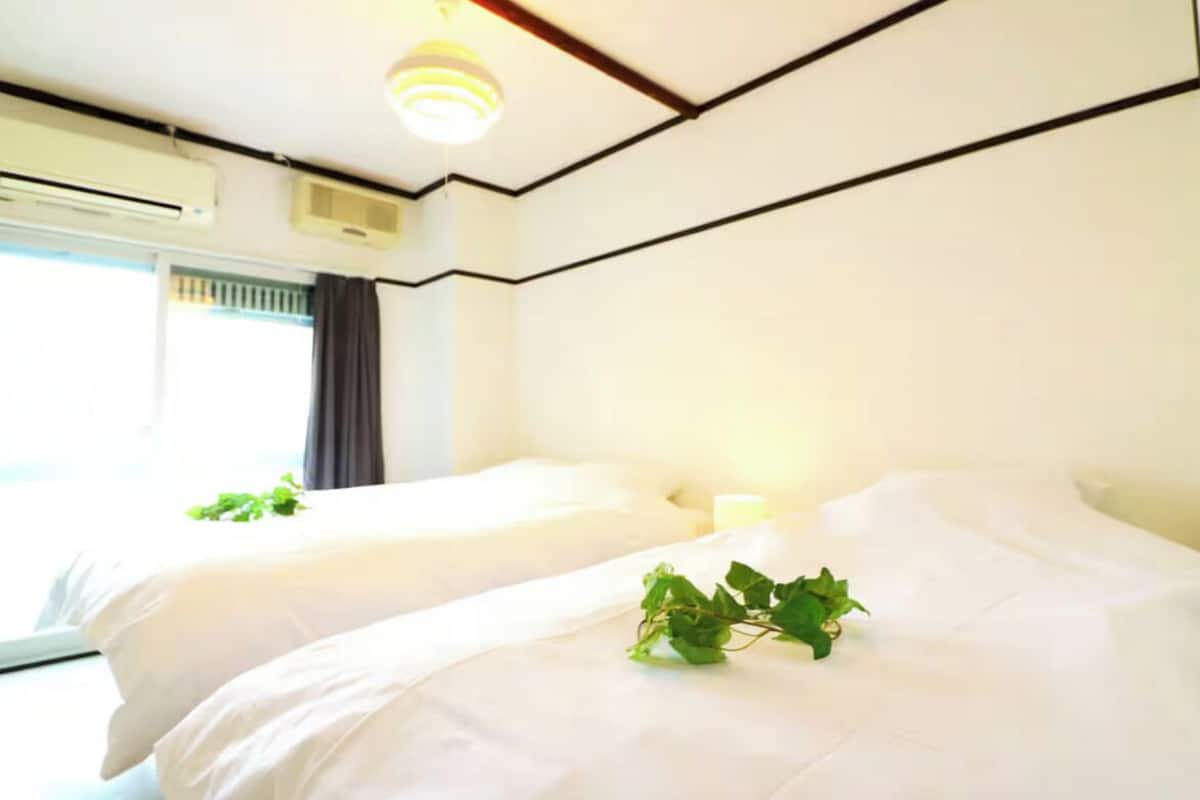 A hotel room with two beds, a window with curtains, an air conditioning unit, and a ceiling light fixture.
