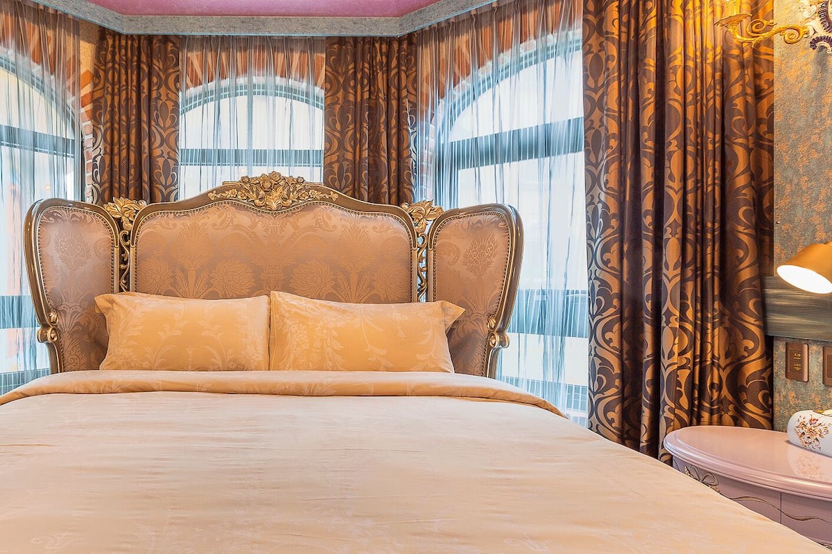 A large bed with ornate headboard, two bedside tables, and curtains with a floral pattern.
