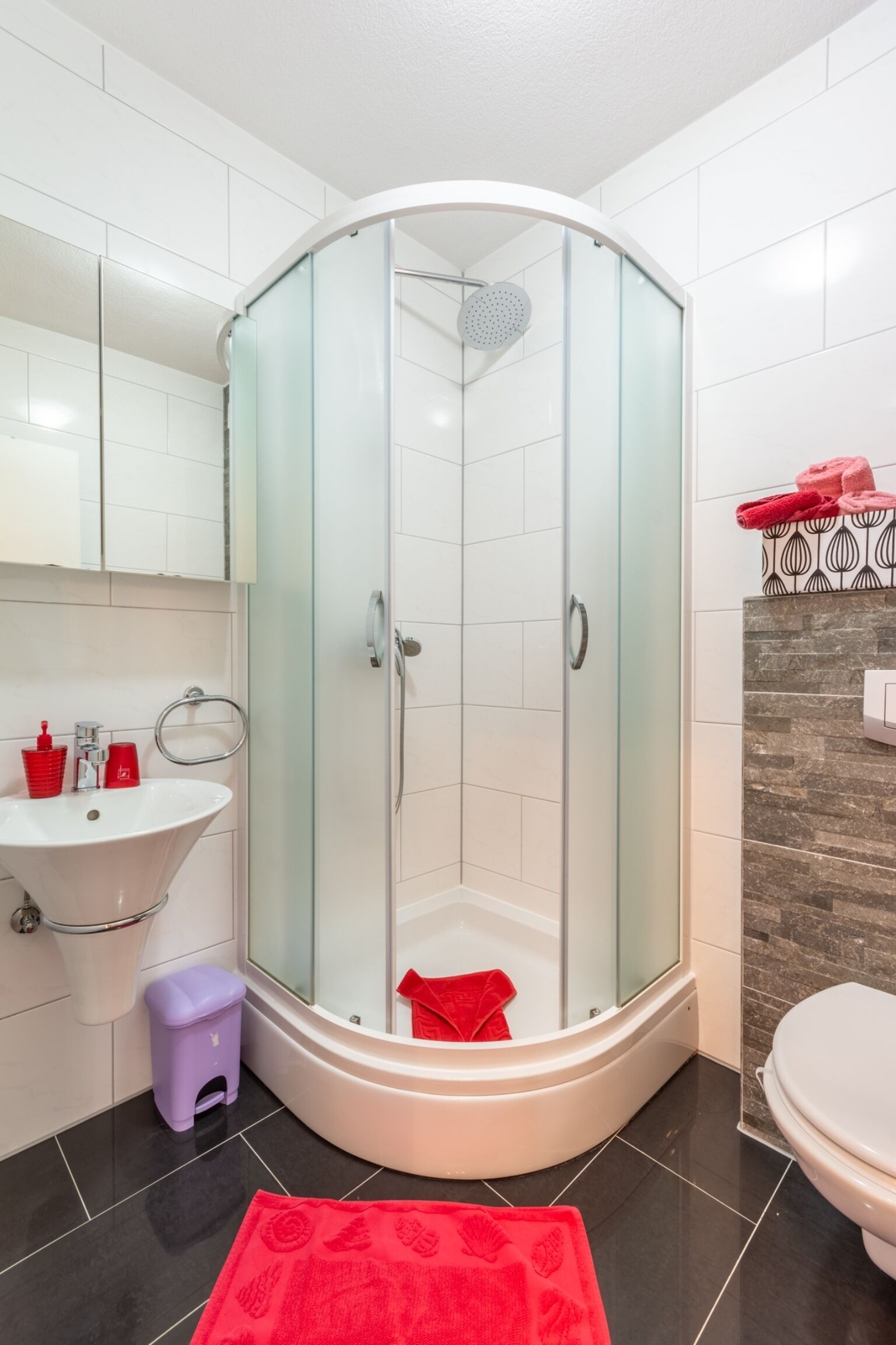 A modern bathroom with a glass-enclosed shower, a white sink, and a small purple stool.