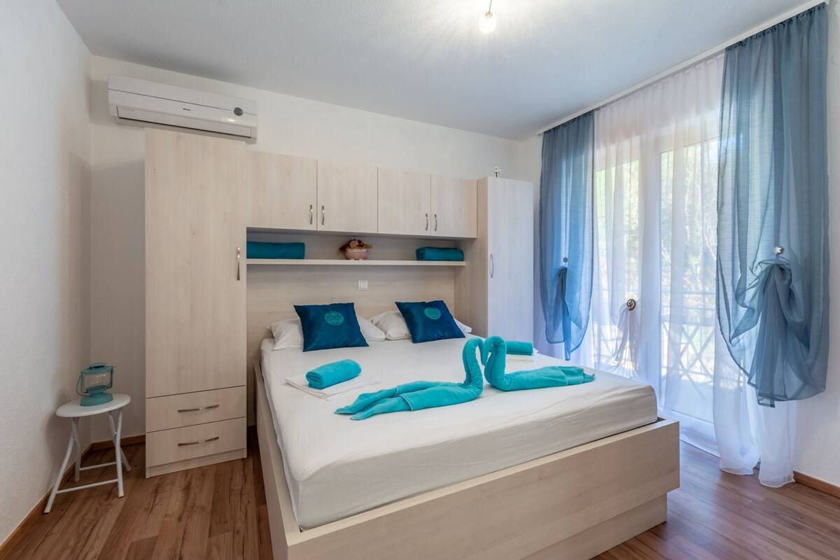 Un dormitorio con cama, armario, mesita y ventana con cortinas.