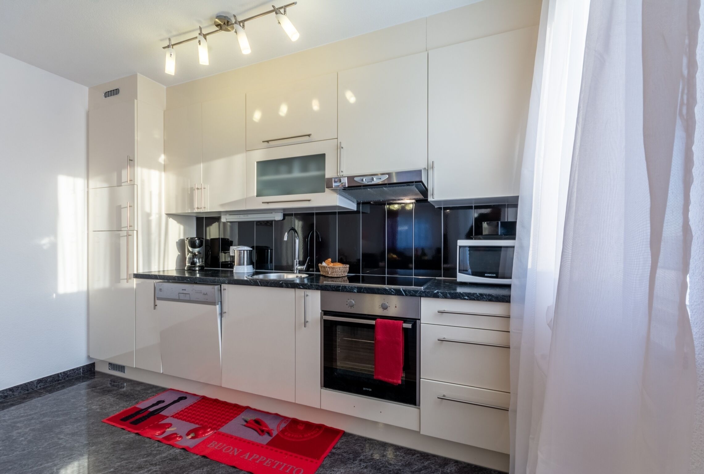 A modern kitchen with white cabinets, a black countertop, a built-in oven, and a microwave.