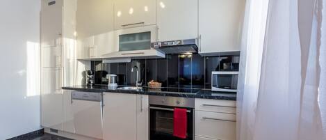 A modern kitchen with white cabinets, a black countertop, a built-in oven, and a microwave.