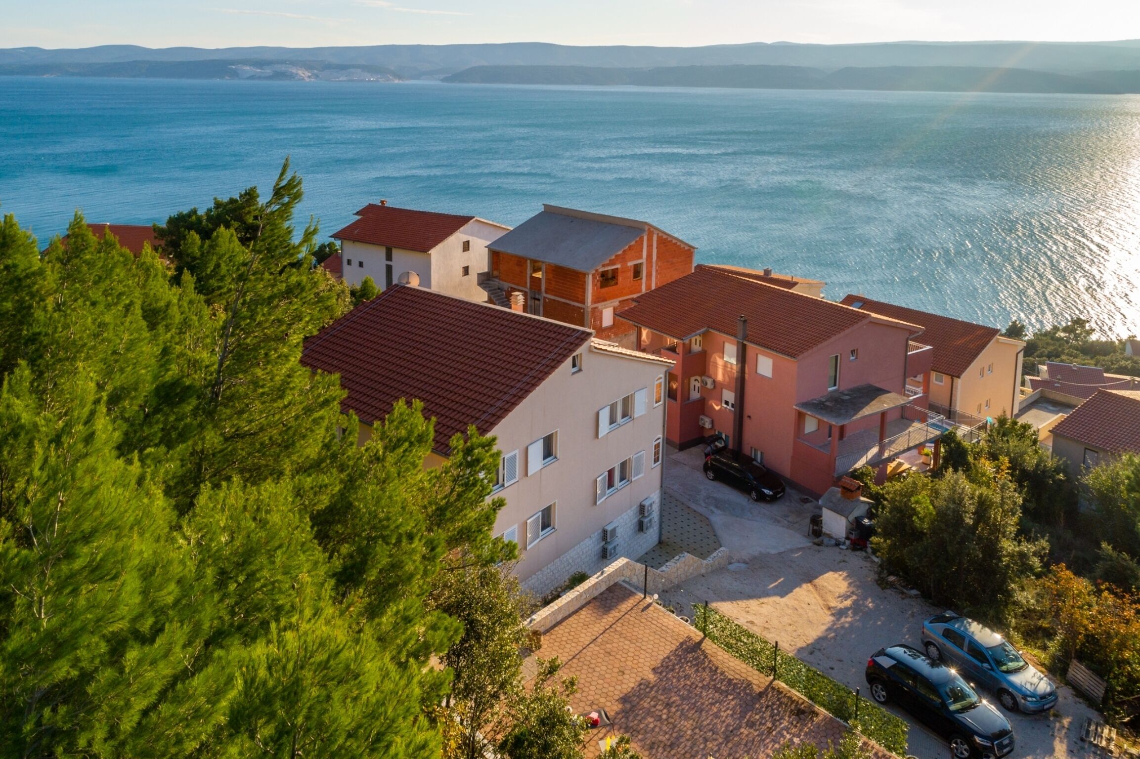 A coastal residential area with buildings, a parking lot, and a view of the sea.