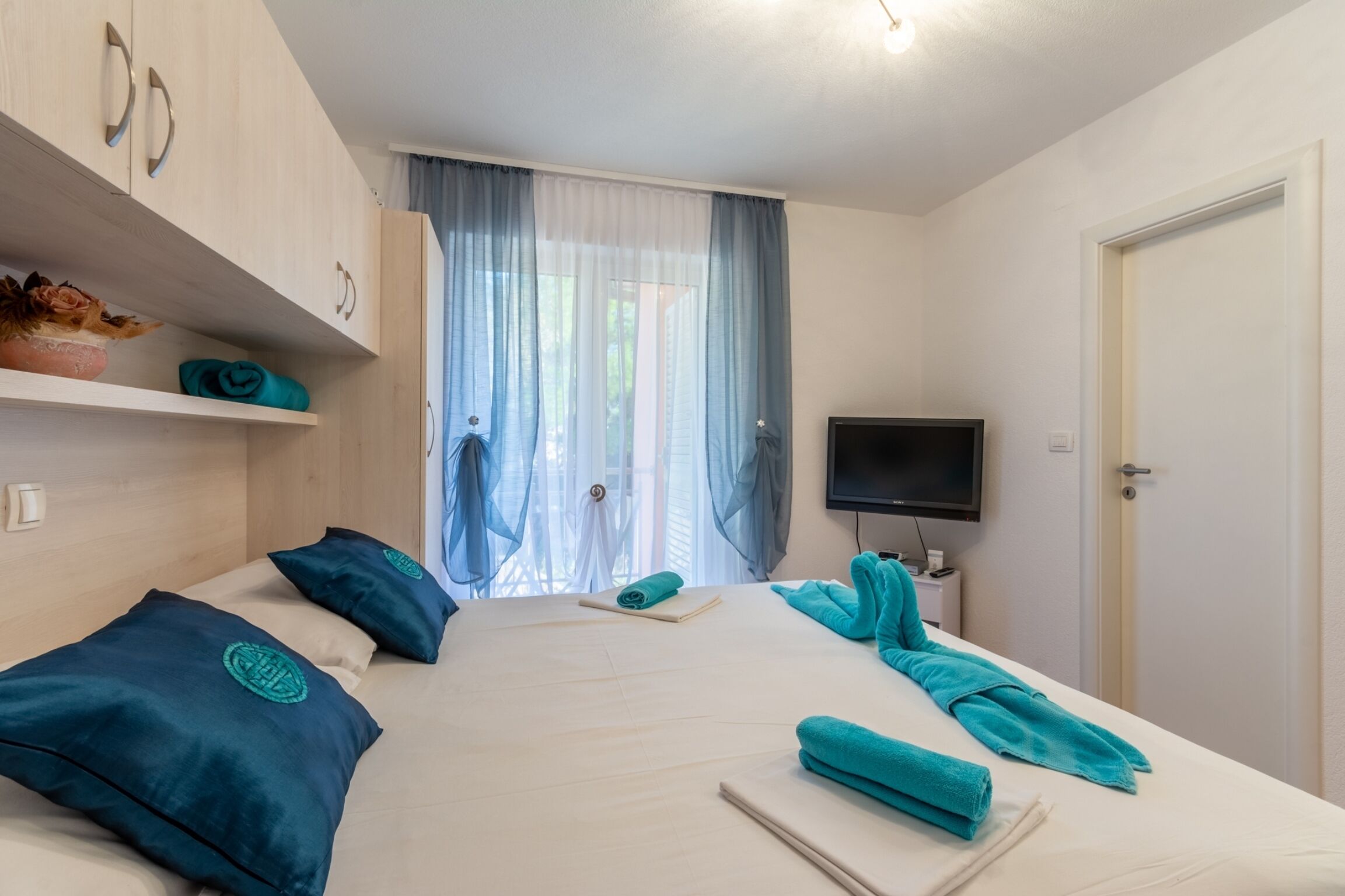 A hotel room with a bed, a TV, a wardrobe, and a window with curtains.
