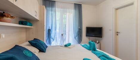 A hotel room with a bed, a TV, a wardrobe, and a window with curtains.