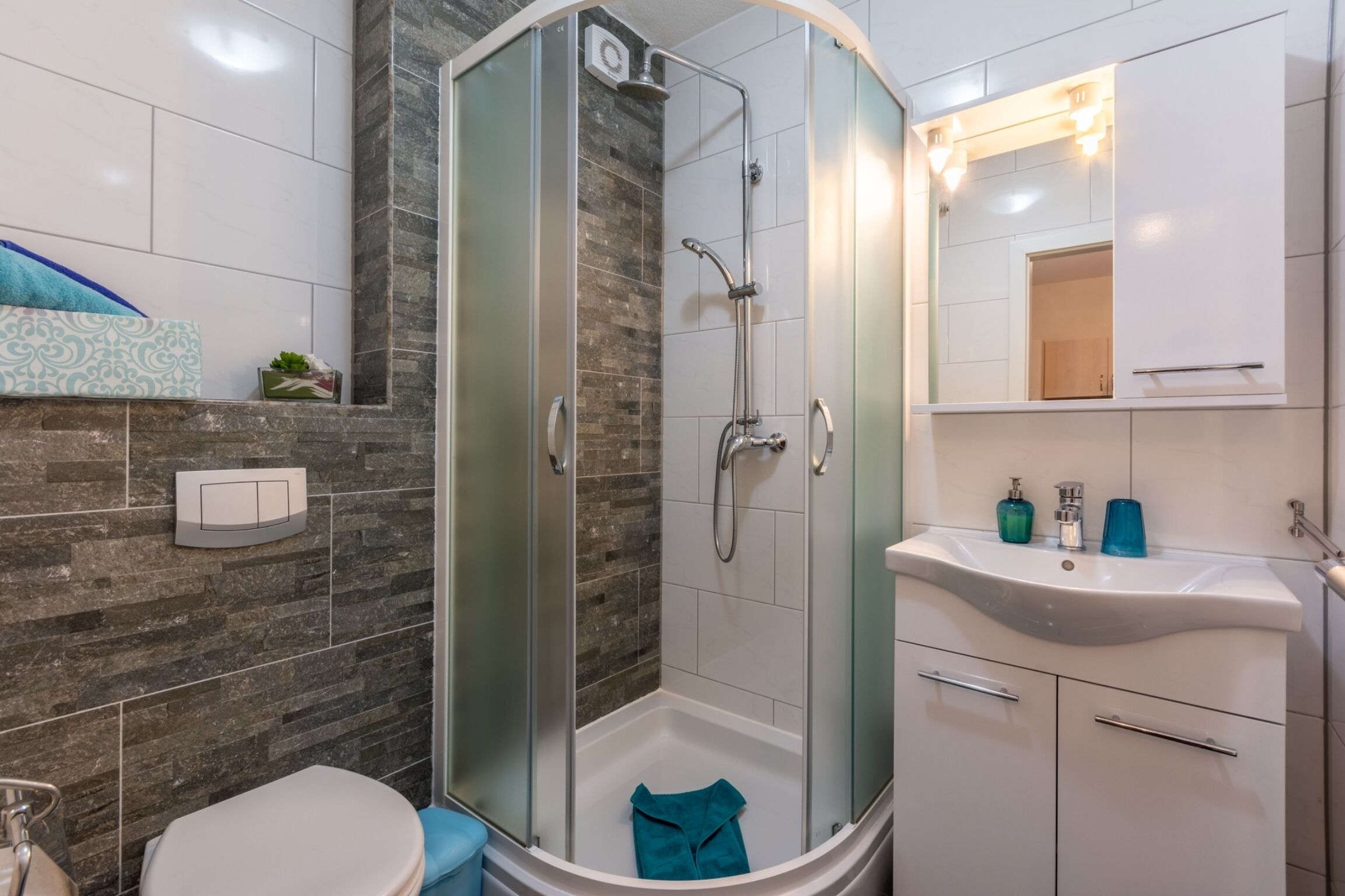 A modern bathroom with a glass-enclosed shower, a white sink with a mirror, and a toilet.