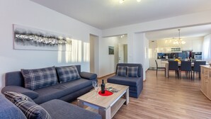 A modern living room with a sofa set, a coffee table, and a dining area with chairs and a table. - Apartments Palma (Omis)