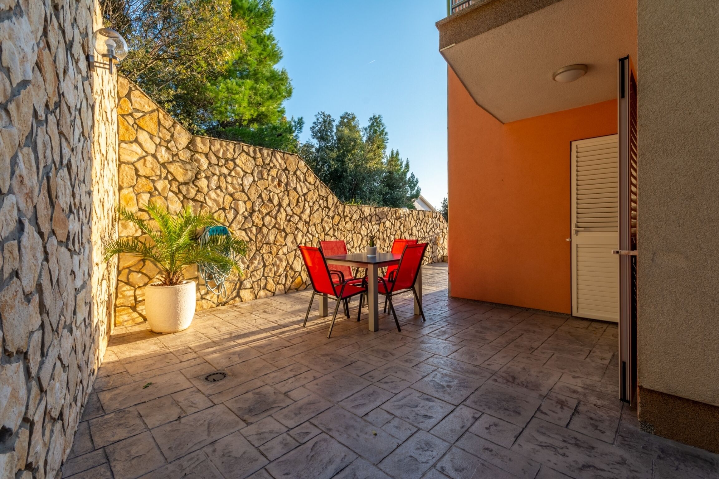 A patio with stone walls, a potted plant, and a table with red chairs.