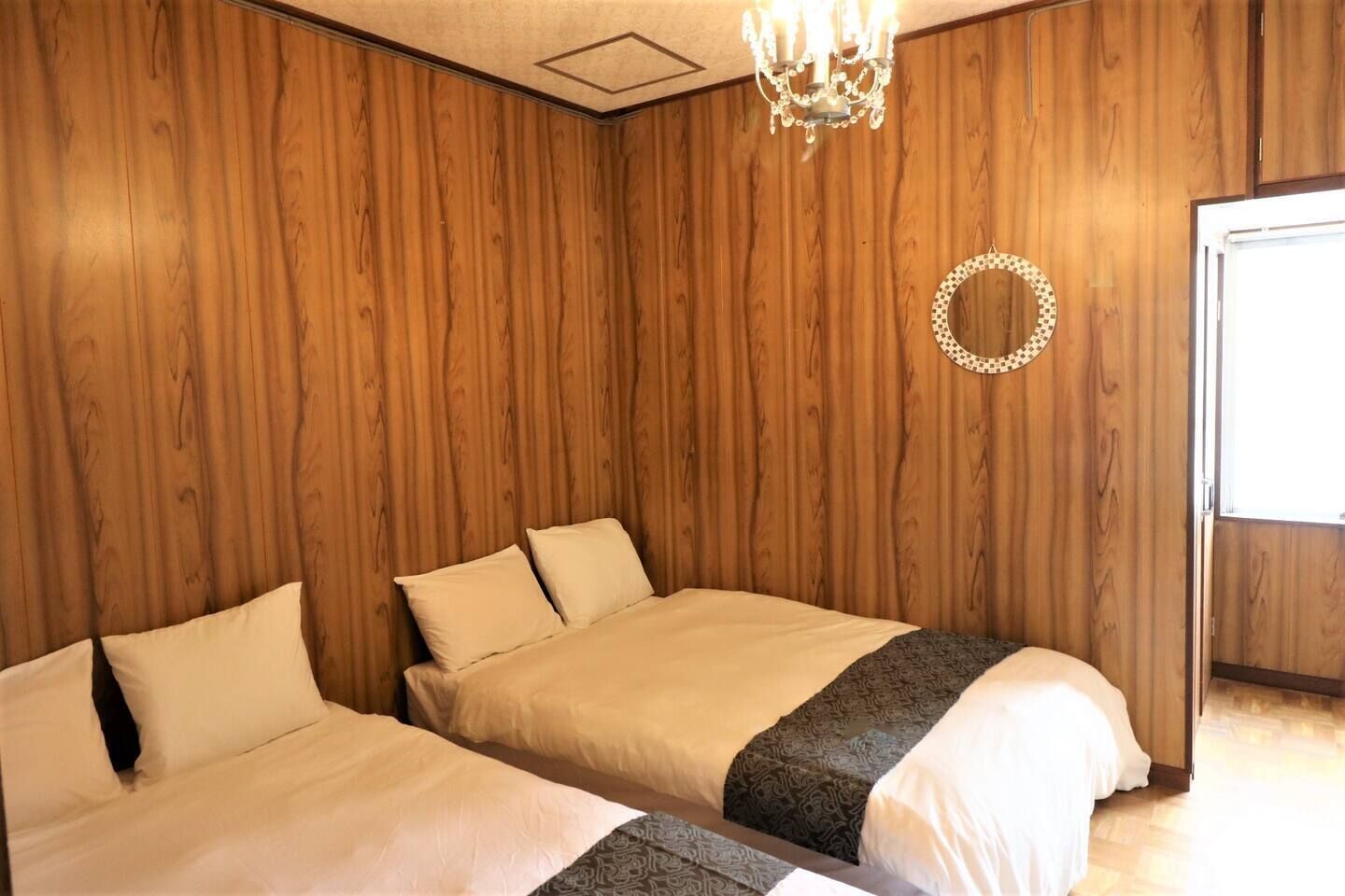 Une chambre avec deux lits, des murs lambrés et un lustre, ainsi qu’un grand miroir rond.