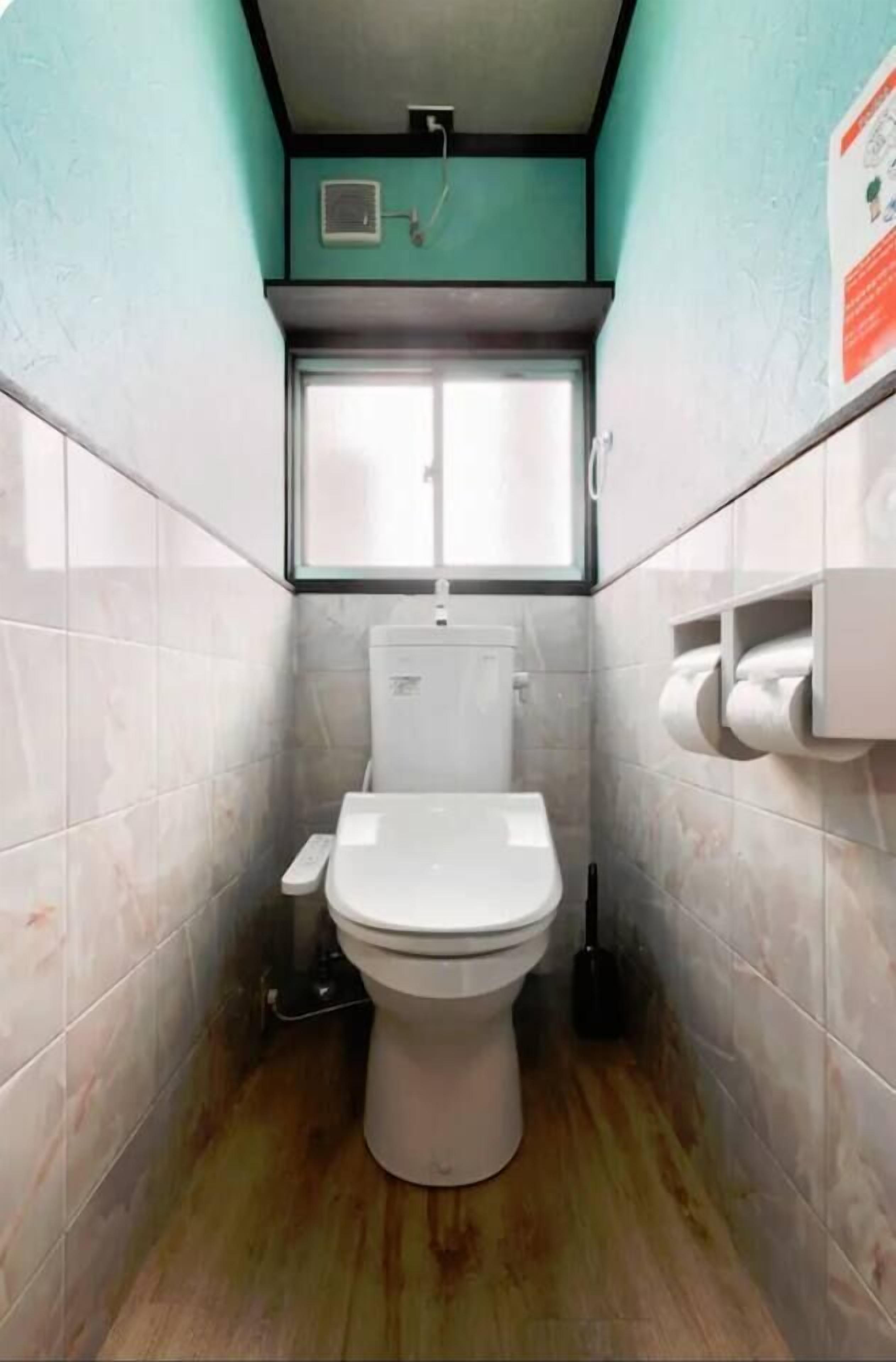 A small, narrow bathroom with a toilet, a window, and a wall-mounted toilet paper holder.