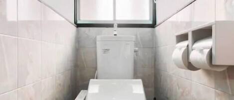 A small, narrow bathroom with a toilet, a window, and a wall-mounted toilet paper holder.