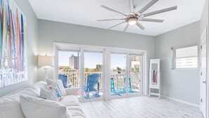 A spacious room with a white ceiling fan, a white couch with decorative pillows, and a view of a deck with outdoor furniture. - Modern Townhome, Short Walk to Beach w/ Private Access, Pool & Grill (Destin)