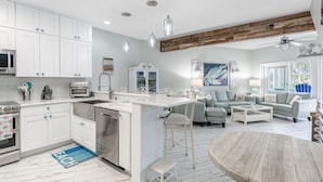 A modern kitchen with white cabinets, a central island, and a dining area with a round table. - Modern Townhome, Short Walk to Beach w/ Private Access, Pool & Grill (Destin)