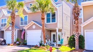 A residential building with multiple garage doors, a front porch with outdoor seating, and palm trees. - Modern Townhome, Short Walk to Beach w/ Private Access, Pool & Grill (Destin)